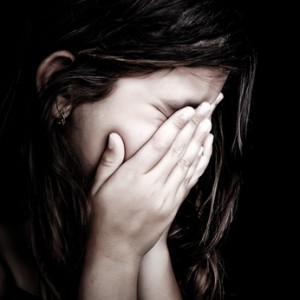Grunge close-up portrait of a girl crying and covering her face isolated on black